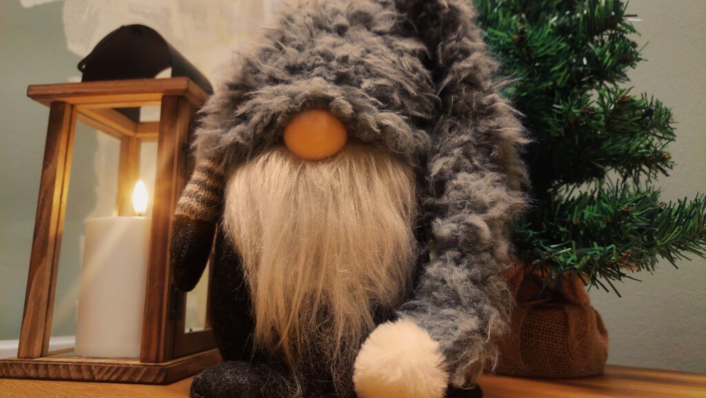 Harmaamyssyinen tonttu seisoo pienen joulukuusen vieressä