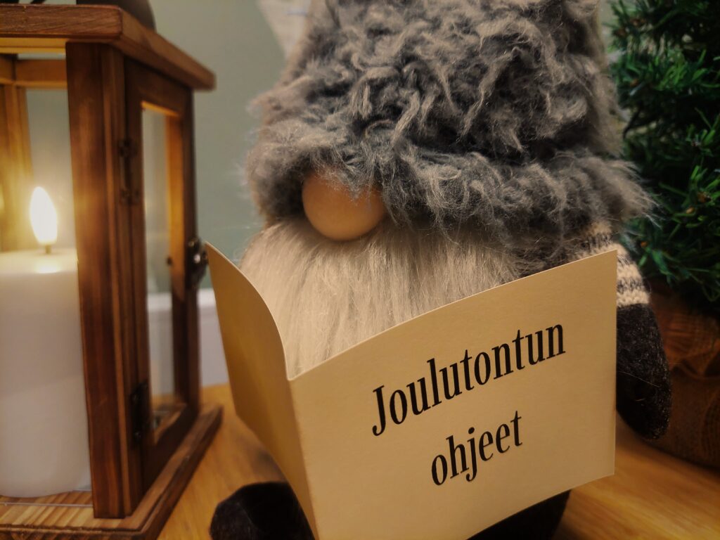 Harmaamyssyinen tonttu lukee Joulutontun ohjeet -kirjaa